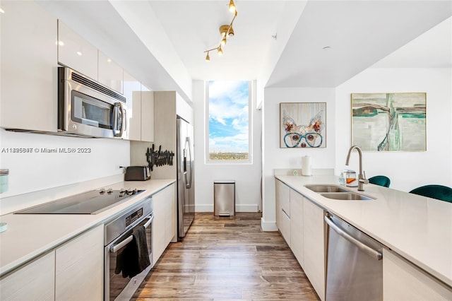 kitchen featuring sink, white cabinets, appliances with stainless steel finishes, wood-type flooring, and track lighting