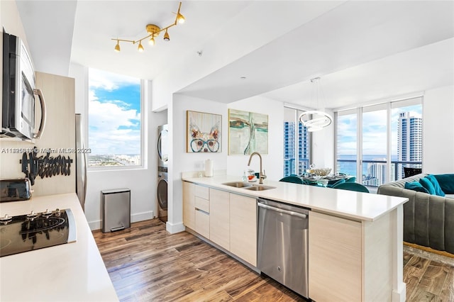 kitchen with appliances with stainless steel finishes, stacked washer and clothes dryer, wood-type flooring, and sink