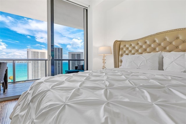 bedroom featuring floor to ceiling windows, a water view, and hardwood / wood-style flooring