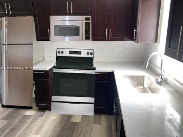 kitchen with appliances with stainless steel finishes, dark brown cabinets, light hardwood / wood-style floors, and sink