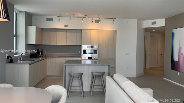 kitchen with stainless steel double oven, light hardwood / wood-style floors, a kitchen island, and light brown cabinets