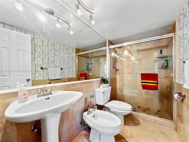 bathroom with toilet, a bidet, tile floors, and tile walls