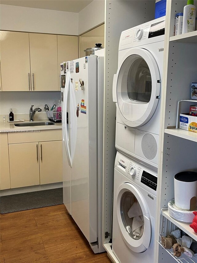 clothes washing area with dark hardwood / wood-style flooring, stacked washing maching and dryer, and sink