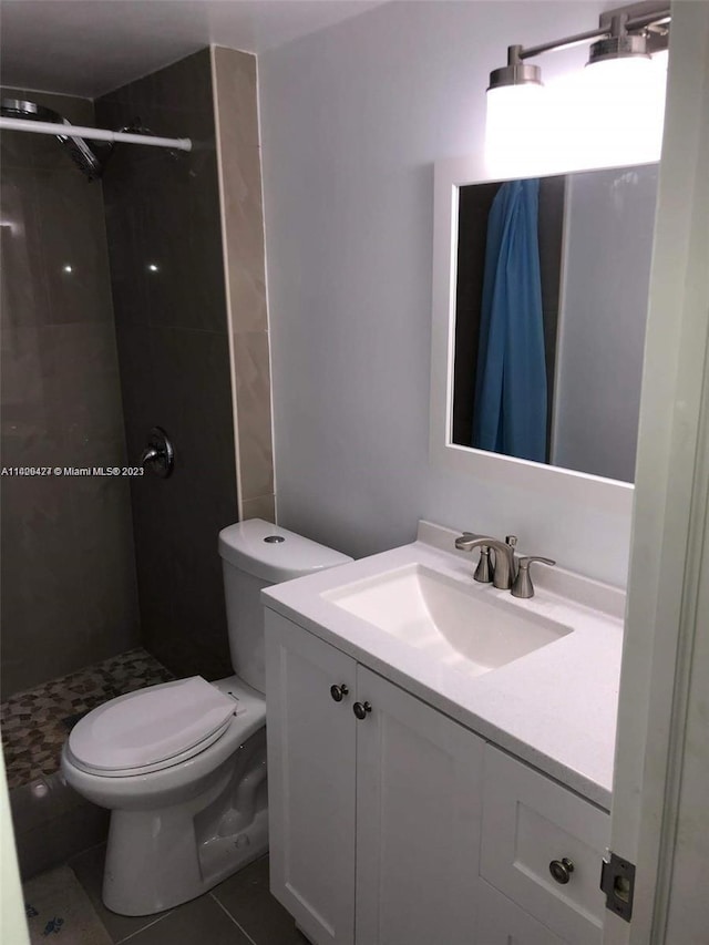 bathroom with tile flooring, oversized vanity, toilet, and tiled shower