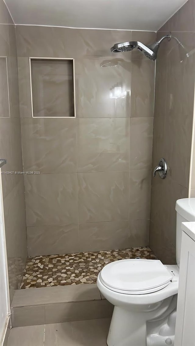 bathroom with toilet, a tile shower, tile floors, and vanity