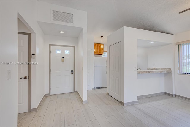 interior space featuring a textured ceiling, white refrigerator, light wood-type flooring, and pendant lighting