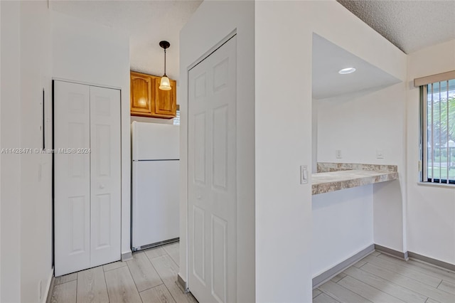 kitchen with light hardwood / wood-style floors, hanging light fixtures, white fridge, and a textured ceiling