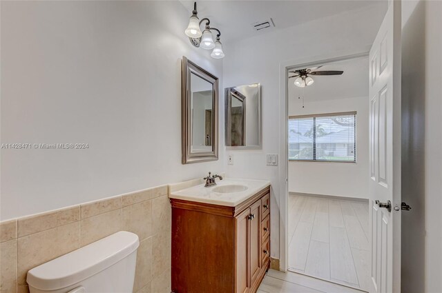 bathroom featuring tile floors, tile walls, vanity with extensive cabinet space, ceiling fan, and toilet