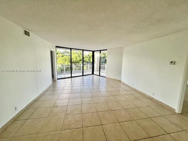 empty room featuring light tile patterned floors, a textured ceiling, visible vents, baseboards, and expansive windows