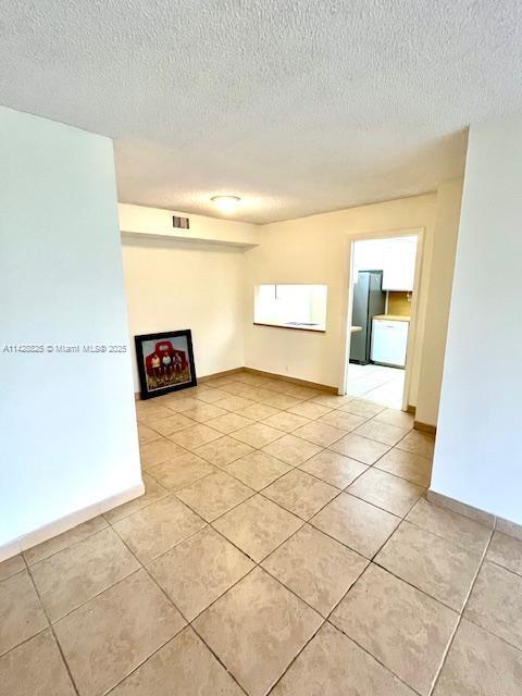 empty room with a textured ceiling, light tile patterned flooring, visible vents, and baseboards