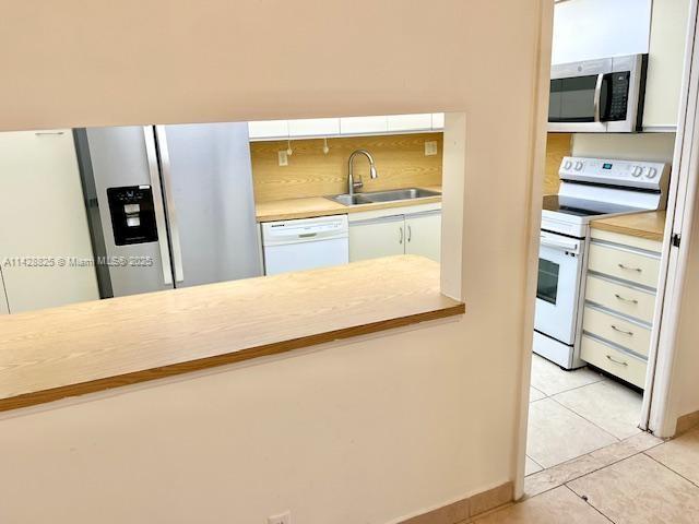 kitchen with light tile patterned floors, stainless steel appliances, light countertops, decorative backsplash, and a sink