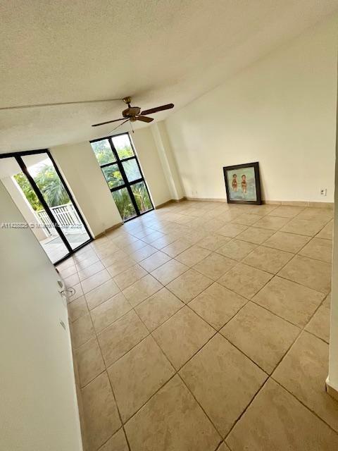 spare room featuring lofted ceiling, a healthy amount of sunlight, a textured ceiling, and light tile patterned floors