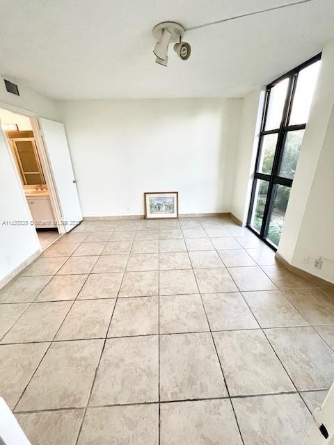 unfurnished room featuring floor to ceiling windows, light tile patterned flooring, visible vents, and baseboards