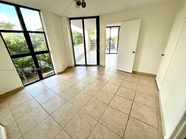 empty room featuring light tile patterned floors, baseboards, and a wall of windows