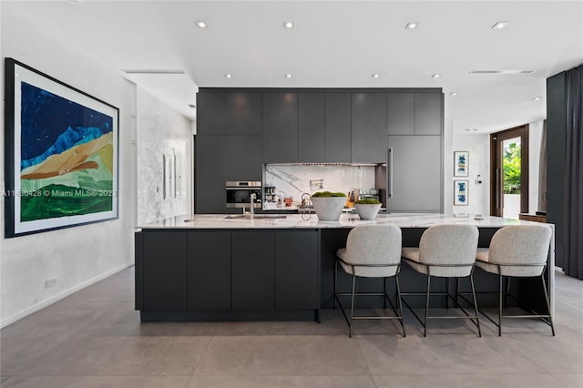 kitchen featuring gray cabinetry, stainless steel oven, a kitchen bar, and sink