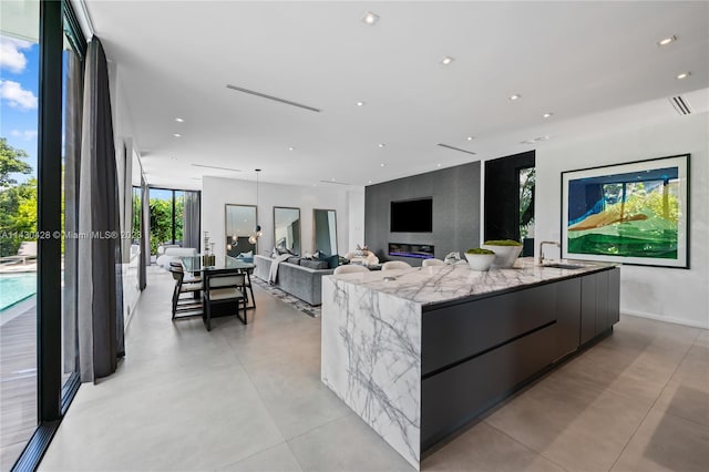 kitchen with light stone counters, sink, a spacious island, and a wall of windows