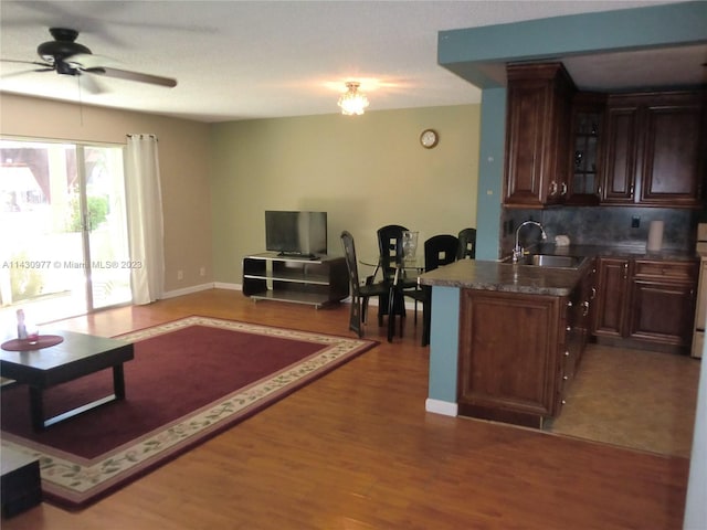 kitchen with dark countertops, decorative backsplash, glass insert cabinets, a sink, and wood finished floors