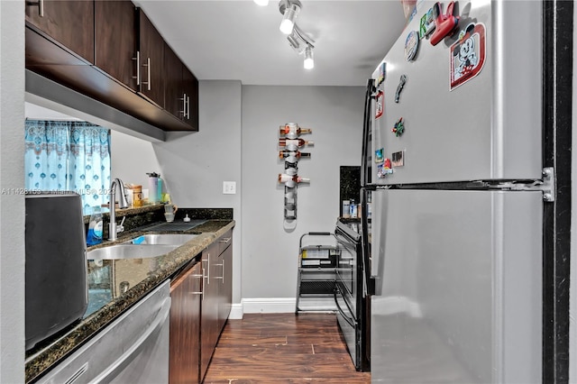 kitchen featuring dark wood-type flooring, track lighting, sink, stainless steel appliances, and dark stone counters