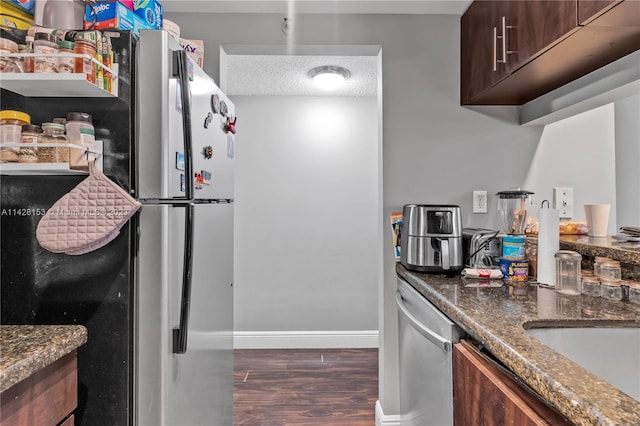 kitchen with dark brown cabinets, dark hardwood / wood-style flooring, appliances with stainless steel finishes, dark stone countertops, and a textured ceiling