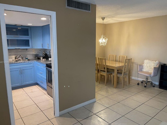 kitchen featuring blue cabinets, light tile floors, backsplash, range, and an inviting chandelier