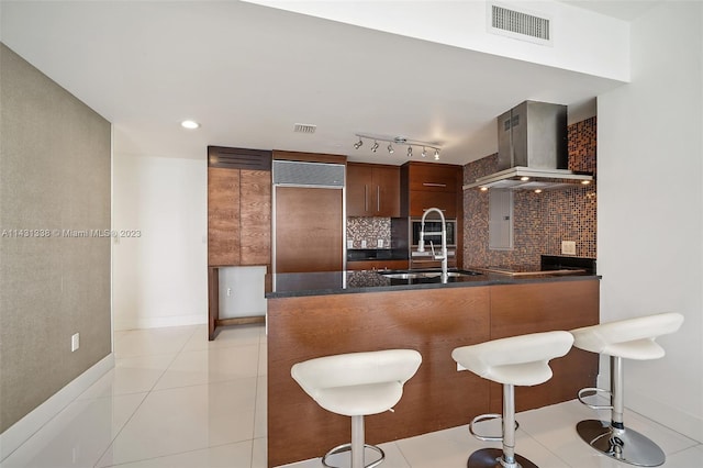 kitchen with rail lighting, a breakfast bar, backsplash, a fireplace, and wall chimney exhaust hood