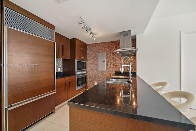 kitchen featuring tasteful backsplash, built in appliances, rail lighting, wall chimney range hood, and sink