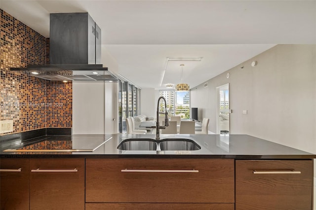 kitchen featuring decorative light fixtures, backsplash, wall chimney range hood, and sink