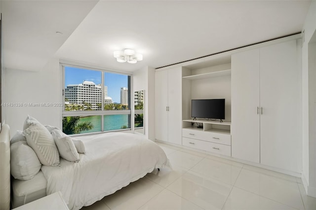 bedroom featuring an inviting chandelier, a water view, and light tile flooring