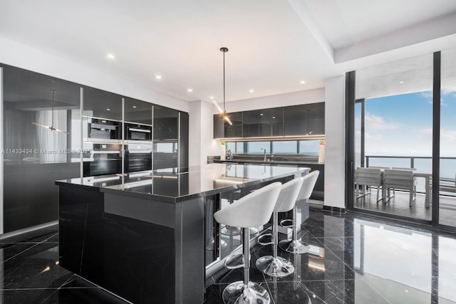 kitchen featuring dark tile floors, pendant lighting, a kitchen bar, and an island with sink