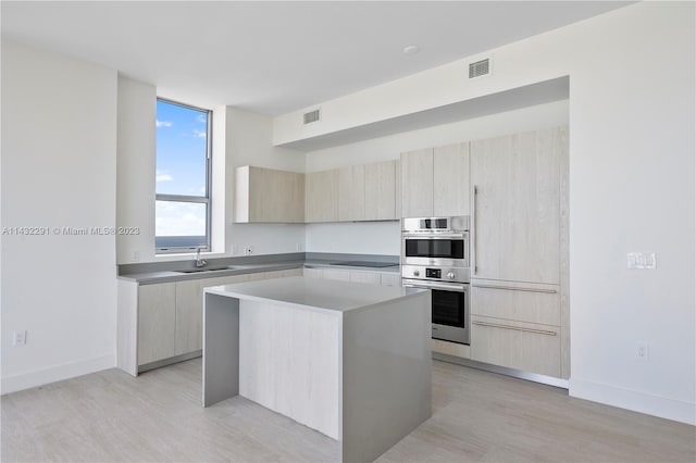 kitchen with a center island, black electric stovetop, stainless steel double oven, light wood-type flooring, and sink