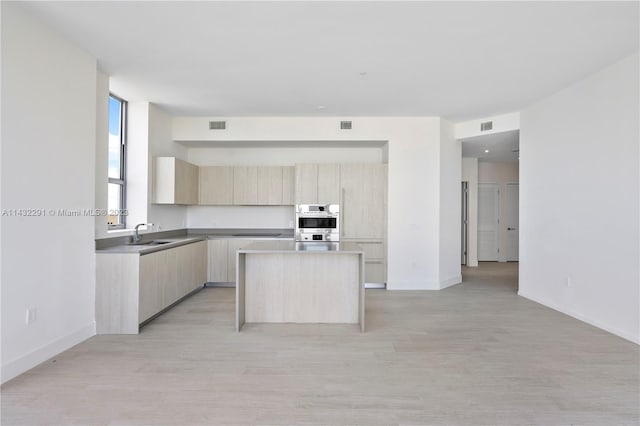 kitchen featuring light brown cabinets, a center island, stainless steel double oven, and light hardwood / wood-style flooring