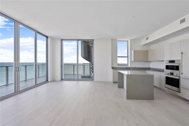 kitchen with floor to ceiling windows, a kitchen island, light hardwood / wood-style floors, double oven, and a water view