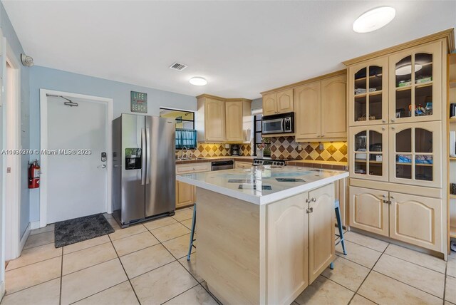 kitchen featuring light brown cabinetry, a kitchen island with sink, appliances with stainless steel finishes, a breakfast bar, and tasteful backsplash