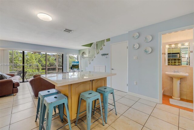 kitchen featuring a kitchen island, a kitchen bar, sink, and light tile floors