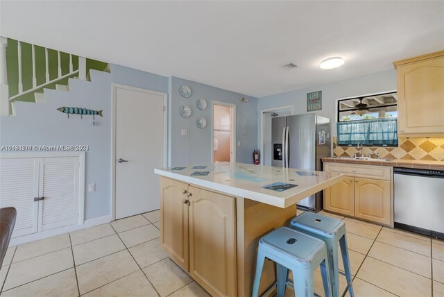 kitchen featuring light brown cabinetry, tasteful backsplash, stainless steel appliances, and a center island