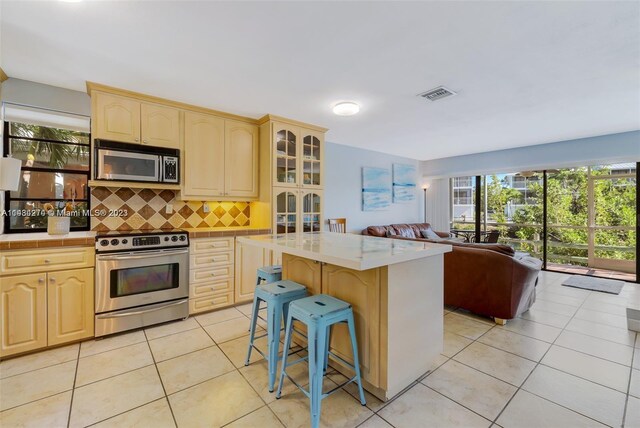 kitchen with light tile floors, a kitchen island, a kitchen breakfast bar, appliances with stainless steel finishes, and tasteful backsplash