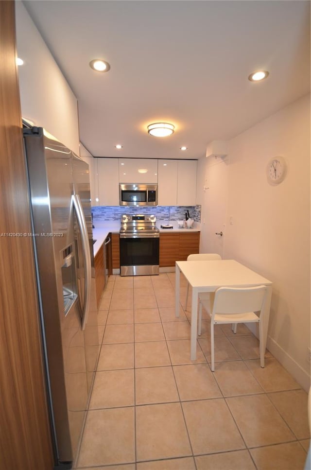 kitchen with backsplash, white cabinets, appliances with stainless steel finishes, and light tile floors