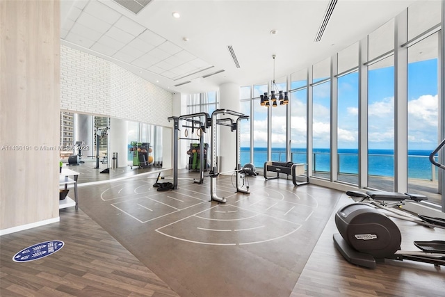 exercise room featuring a wall of windows, a chandelier, a high ceiling, a water view, and hardwood / wood-style flooring