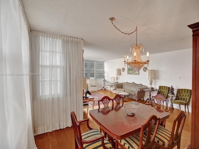 dining space with an inviting chandelier, a textured ceiling, and wood-type flooring