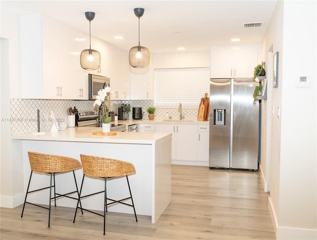 kitchen with light hardwood / wood-style floors, stainless steel appliances, decorative light fixtures, white cabinets, and sink