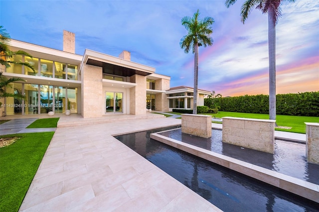 pool at dusk featuring a patio area and a lawn