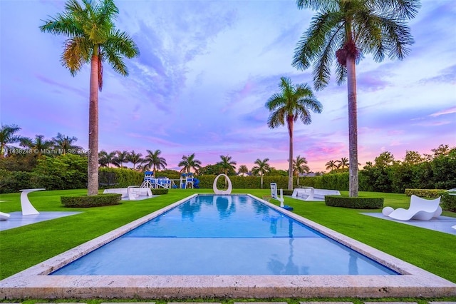 pool at dusk featuring a water slide, a lawn, and a patio area