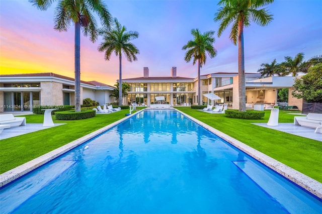 pool at dusk with a patio and a yard