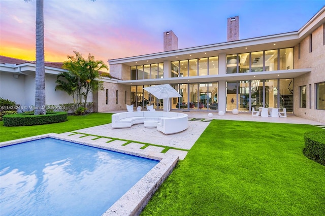 back house at dusk with a swimming pool with hot tub, a yard, and a patio area