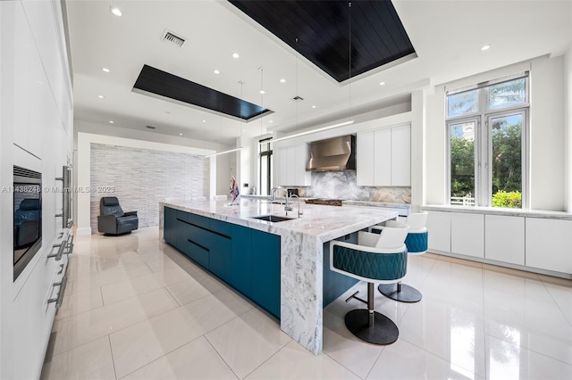 kitchen with a center island with sink, white cabinets, light stone counters, and pendant lighting