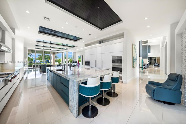 kitchen featuring light stone countertops, white cabinetry, a kitchen island with sink, sink, and light tile floors