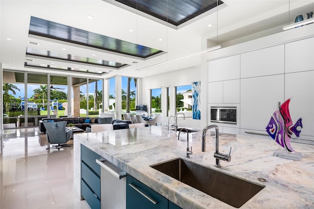 kitchen featuring light stone countertops, a raised ceiling, white cabinetry, and sink