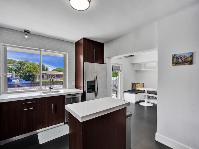 kitchen featuring appliances with stainless steel finishes, dark tile patterned flooring, a center island, sink, and dark brown cabinetry