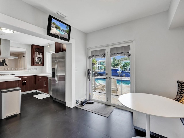 kitchen with wall chimney range hood, french doors, decorative backsplash, appliances with stainless steel finishes, and dark brown cabinetry