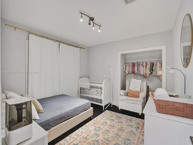 bedroom with dark wood-type flooring, heating unit, track lighting, and a closet